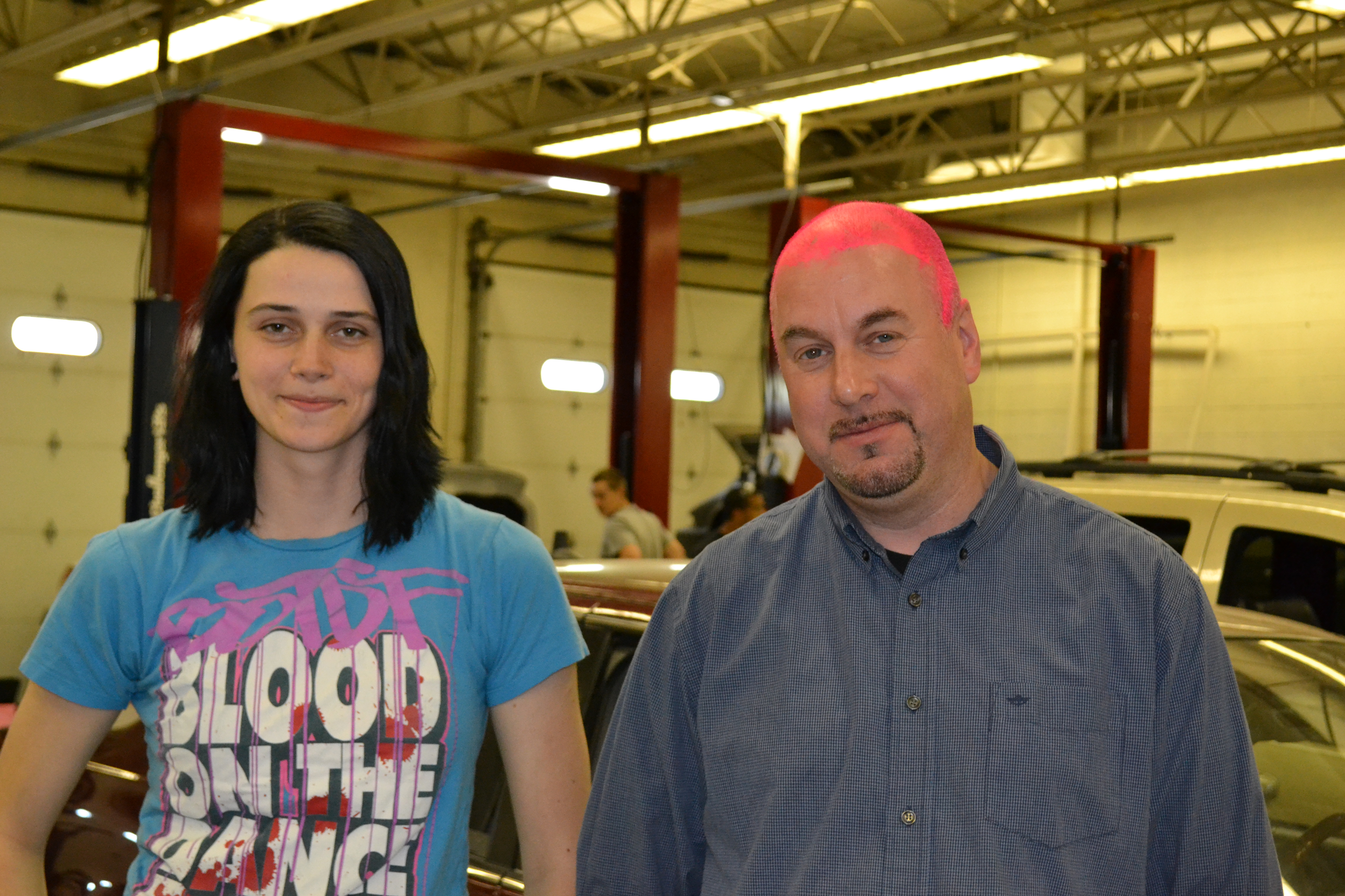 Alex Wolfe stands with her pink haired automotive teacher, Scott Freeman. The two made a bet that if Wolfe placed in the national automotive competition, he would paint his head pink.