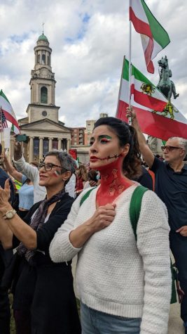 A woman, before the protest march begins, listens to the original Iranian national anthem in solidarity.