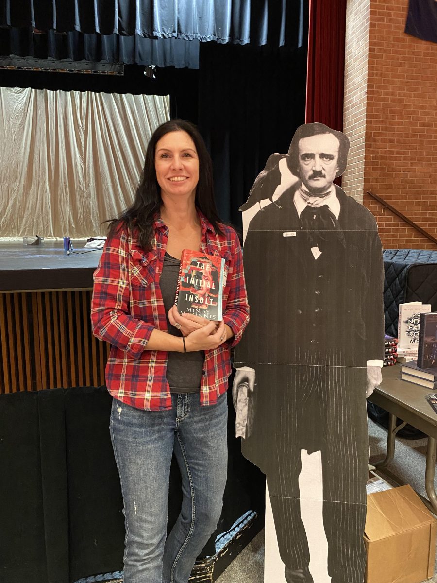 Mindy McGinnis poses in the auditorium with one of her published books along with a cutout of Edgar Allan Poe.