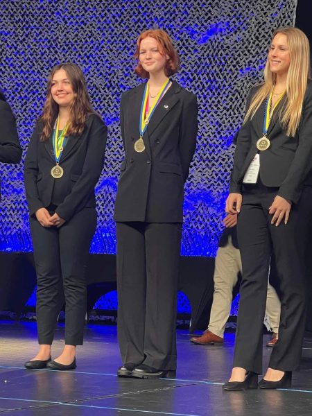Kaitlyn Dysart-Moore (middle) at DECA States on stage with an award for placing in the top 8 in the Restaurant and Food Service Management category.