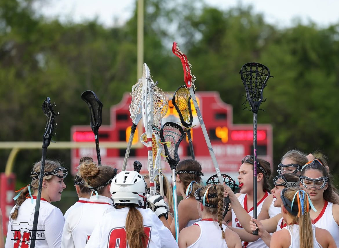 The FHS girls' lacrosse team raising their sticks after finishing a game.