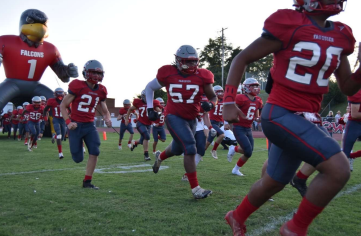 The football team is full of energy as they run out from under the inflatable falcon.