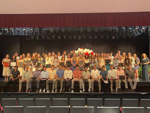 The scholarship recepients stand on stage, holding their scholarships. 